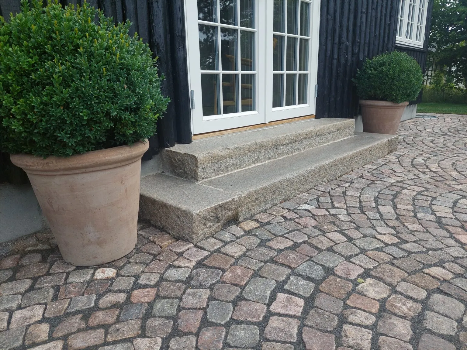 Granittrappe og chaussesten ved sortmalet træhus